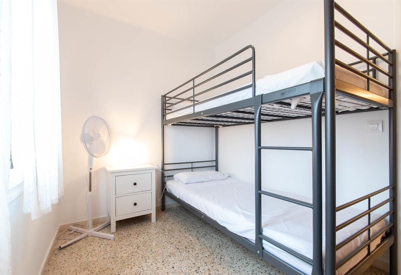 Camera con letto a castello, comodino e ventilatore.