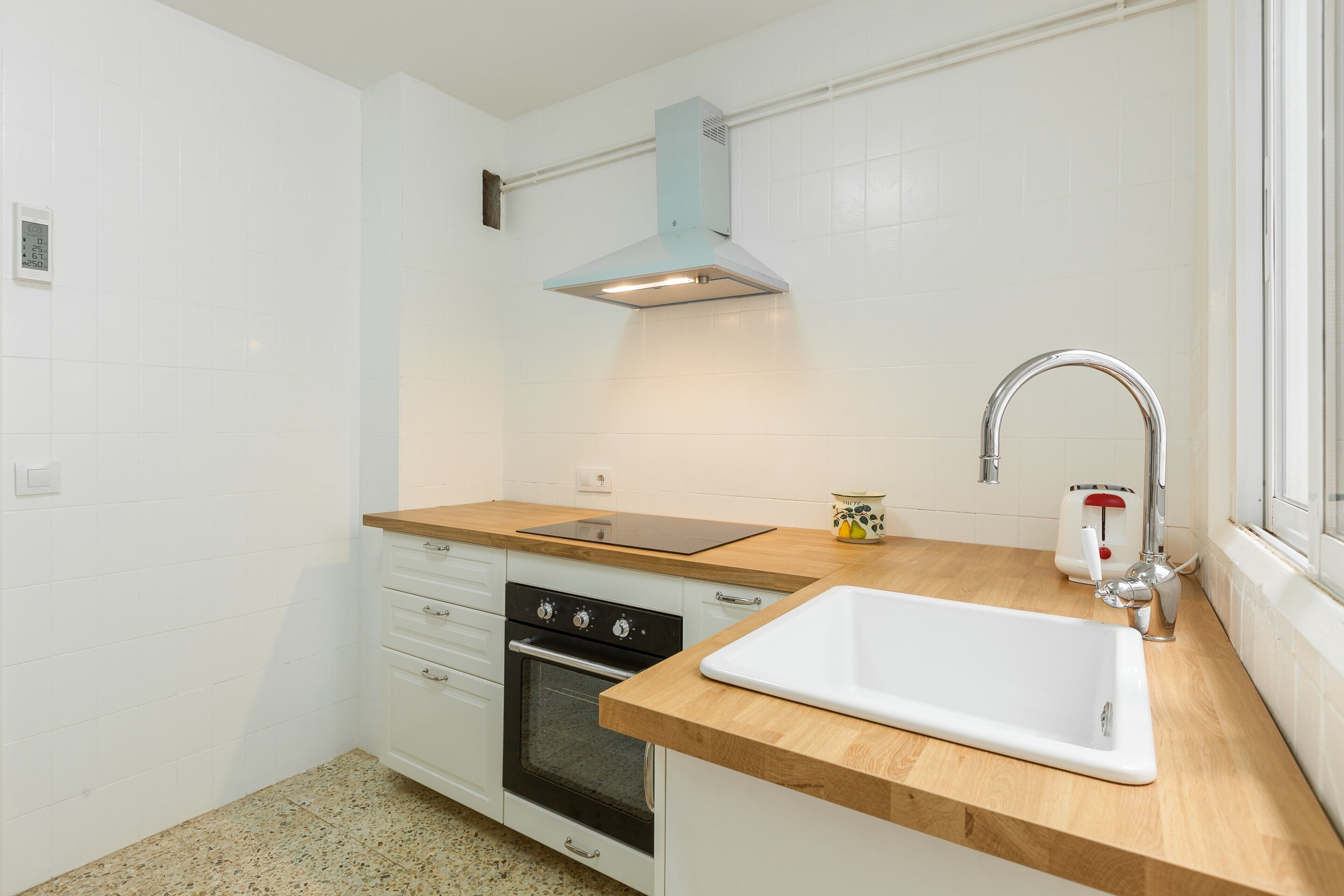 A kitchen with white cabinets, a stainless steel oven, a wooden countertop, a white sink, and a window.