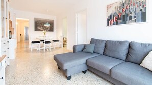 A modern living room with a grey sofa, a dining area with white chairs, and a cityscape painting on the wall.