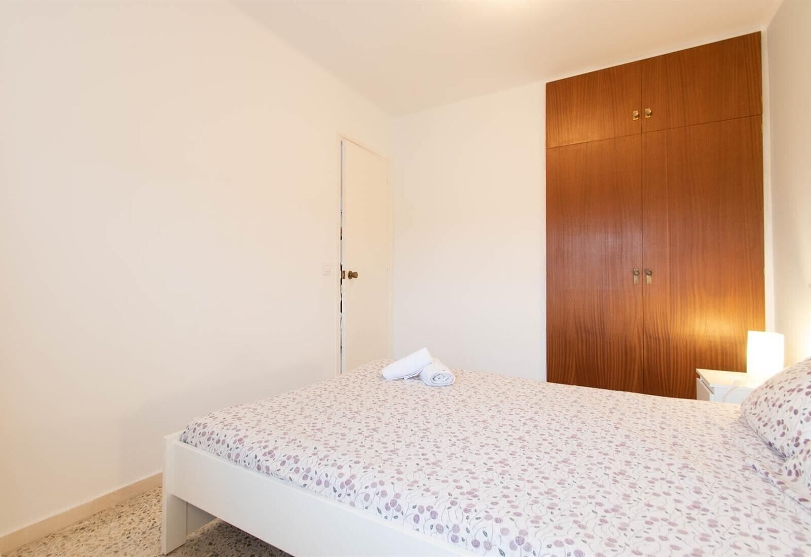 Une chambre à coucher avec un lit, une armoire en bois, une porte et une table de chevet avec une lampe.