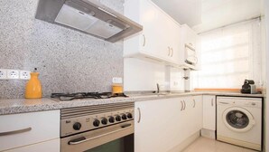 A kitchen with a gas stove, oven, microwave, and a washing machine. - Apartment with Sea View, Terrace, and Beachfront Location (Canet  de mar)