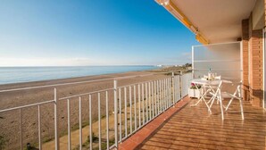 A balcony with a view of the beach and ocean, a table with chairs, and a white railing. - Apartment with Sea View, Terrace, and Beachfront Location (Canet  de mar)