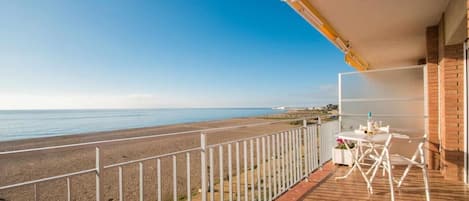 Varanda com vista para a praia e o oceano, uma mesa com cadeiras e guarda-corrimão branco.