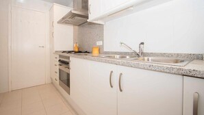 A kitchen with white cabinets, a stainless steel sink, and a stove. - Apartment with Sea View, Terrace, and Beachfront Location (Canet  de mar)