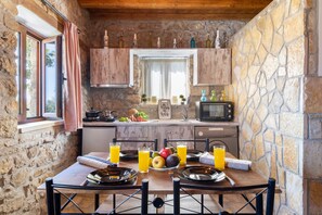 Une cuisine rustique en pierre avec une table à manger dressée pour le petit-déjeuner, comprenant des fruits et du jus d’orange.