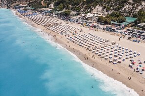 A beach with rows of sunbeds and umbrellas, a sandy shore, and a rocky cliff in the background. - “Villa Lazar” with Terrace, Air Conditioning, and Wi-Fi (Lefkada)