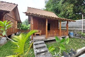 A wooden house with a tiled roof and a porch. There is a bench on the porch and a potted plant nearby. - Mbok Niem Cafe and Cottage (Bangunjiwo)