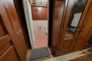 A wooden door leading to a bathroom with a shower, tiled walls, and a visible toilet. - Mbok Niem Cafe and Cottage (Bangunjiwo)