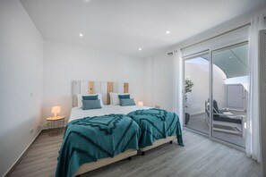 Une chambre à coucher comprenant un lit, des tables de chevet et une porte-fenêtre coulissante donnant sur un espace extérieur.