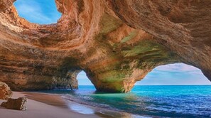 Eine natürliche Felsformation mit einem Bogen über dem Meer, ein Sandstrand und klares, blaues Wasser.