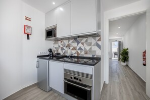 A compact kitchen with a microwave, oven, and built-in stove, white cabinetry, and a geometric tile backsplash.