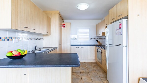 Une cuisine compacte avec des meubles en bois, un plan de travail noir, un évier, une cuisinière et un réfrigérateur blanc.