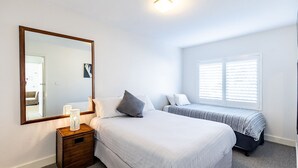 Un dormitorio con un espejo grande, dos camas, una mesita de noche con lámpara y una ventana con persianas.
