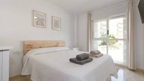 Un dormitorio con cabecera de madera, una cama grande con ropa blanca, dos cuadros en la pared y una ventana con cortinas.