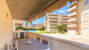 Un patio al aire libre con una mesa y sillas, una piscina al fondo y un edificio con balcones.