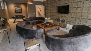 Een moderne woonkamer met een gebogen bank, een salontafel en een flatscreen televisie die aan een gestructureerde muur is bevestigd.