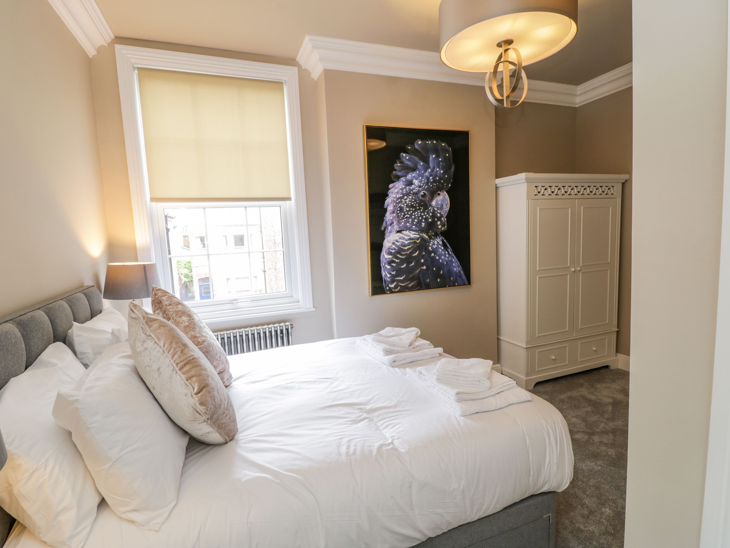 Un dormitorio con una cama grande, una ventana con persiana, un radiador, un armario y una obra de arte colgada en la pared.