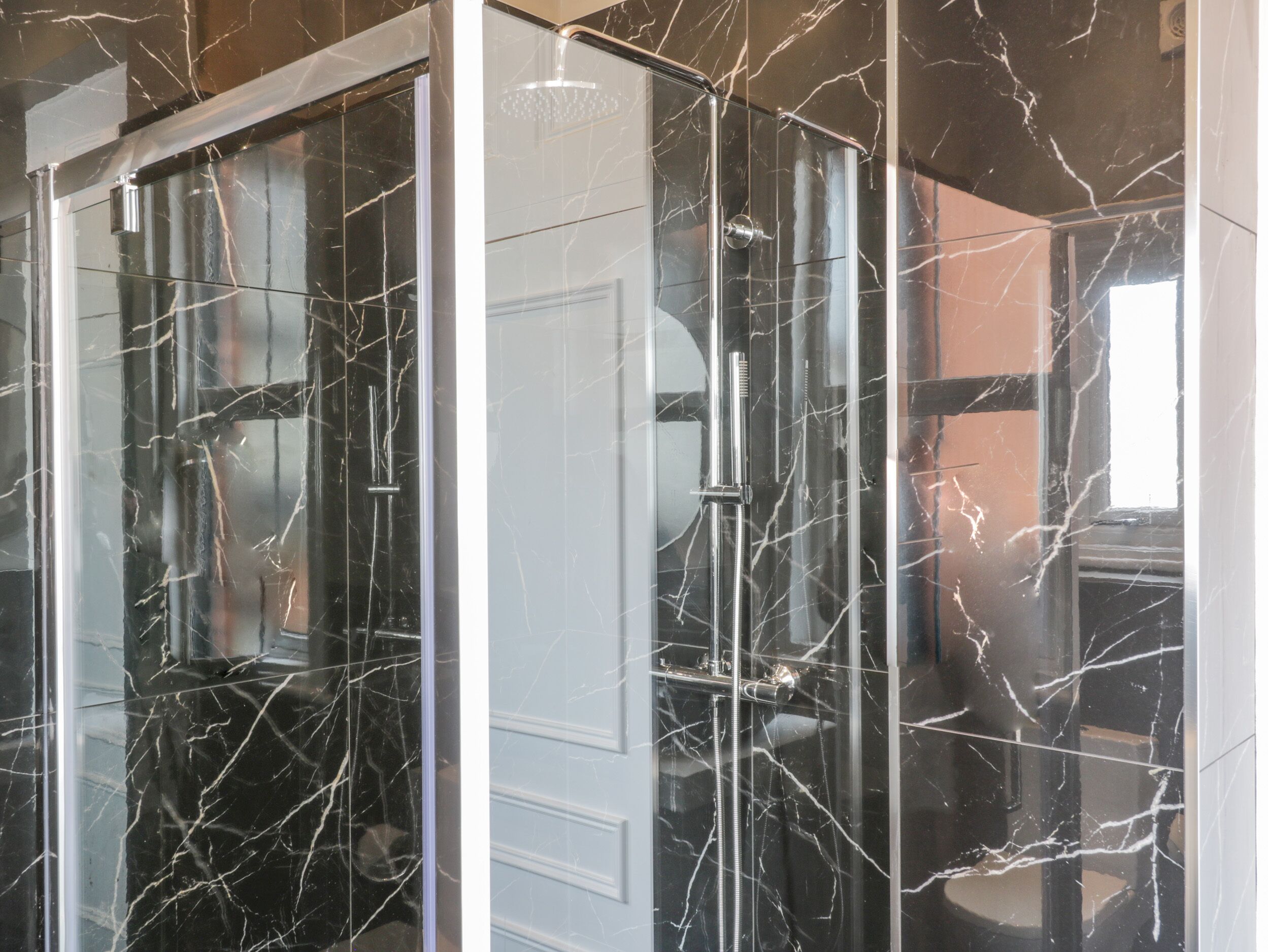 A modern bathroom with a glass-enclosed shower, marble walls, and a visible door.