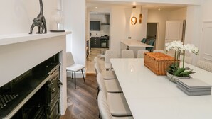 Een moderne keuken met witte kastjes, een eethoek met een witte tafel en stoelen, en een keukeneiland met een mand en orchideeën.