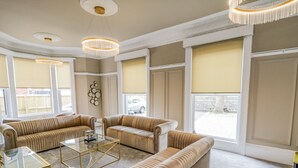 Een ruime woonkamer met beige banken, een glazen salontafel en een kroonluchter.