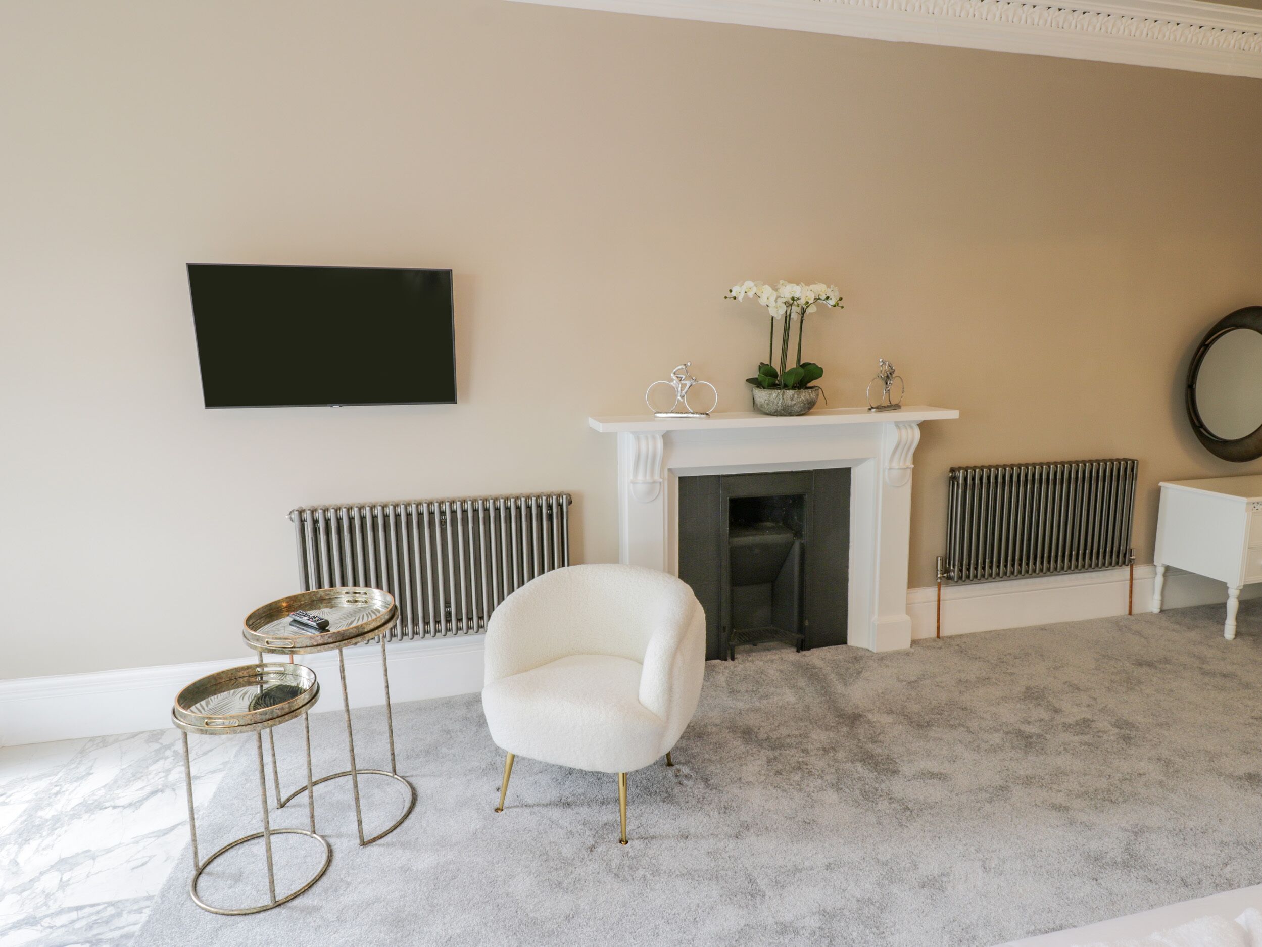 A living room with a white armchair, a fireplace, a radiator, and a television mounted on the wall.
