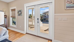 A spacious room with a wooden floor, a large sliding glass door leading to an outdoor deck, and a framed picture on the wall. - Beach House Near Pool and Boardwalk (Cape San Blas)
