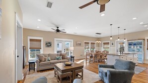 A spacious living room with a large sofa, a dining area with wooden chairs, a kitchen with a central island, and a ceiling fan. - Beach House Near Pool and Boardwalk (Cape San Blas)