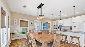 A modern kitchen with white cabinets, a wooden dining table, and hanging pendant lights. - Beach House Near Pool and Boardwalk (Cape San Blas)