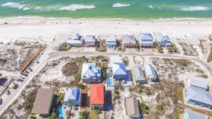 Vista aérea de un complejo turístico costero con varios edificios, una playa y un aparcamiento.