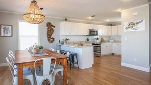 Una cocina moderna con armarios blancos, una isla central y un comedor con mesa de madera y sillas blancas.