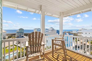 Un balcon abrité avec deux fauteuils Adirondack, une vue sur l’océan et un espace piscine.