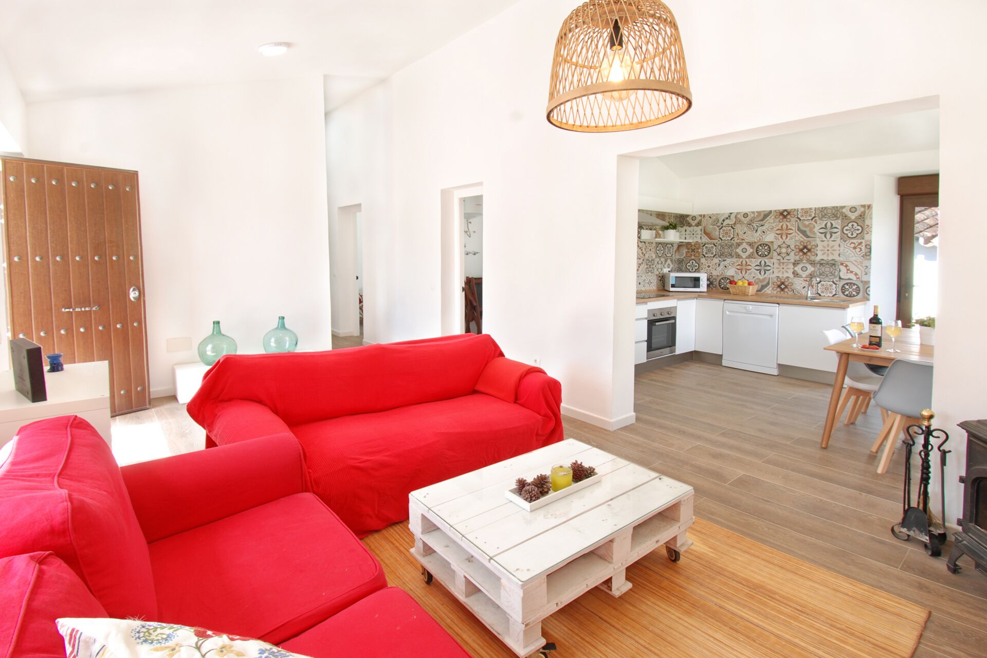 Un salon moderne avec un canapé rouge, une table basse blanche et une cuisine en arrière-plan.