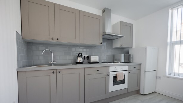 A modern kitchen with grey cabinets, a stainless steel sink, a microwave, and a built-in oven. - Platform Stadium Apartment (Hull)