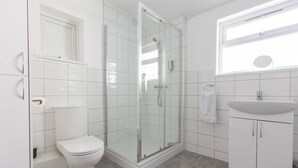 A modern bathroom with a glass-enclosed shower, a white toilet, and a sink with a mirror above it. - Platform Stadium Apartment (Hull)