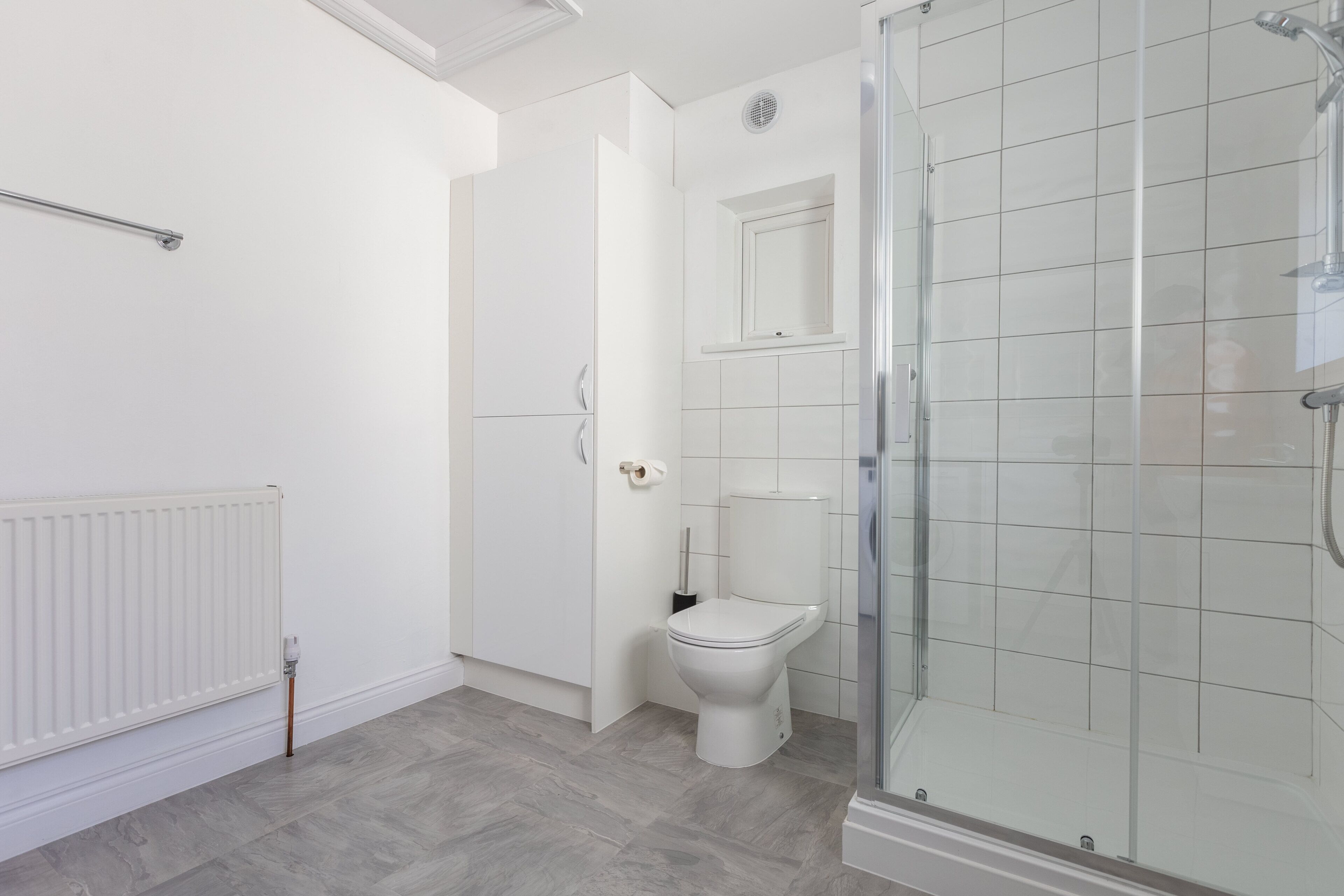 A modern bathroom with a toilet, a glass shower enclosure, and a white radiator.