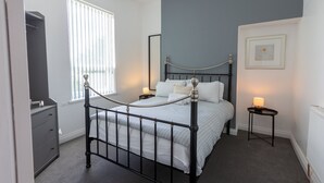 A bedroom with a bed, bedside tables, a dresser, and a window with blinds. - Platform Stadium Apartment (Hull)