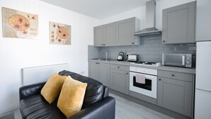 A modern kitchen with grey cabinets, a black leather sofa with yellow cushions, and a white radiator. - Platform Stadium Apartment (Hull)