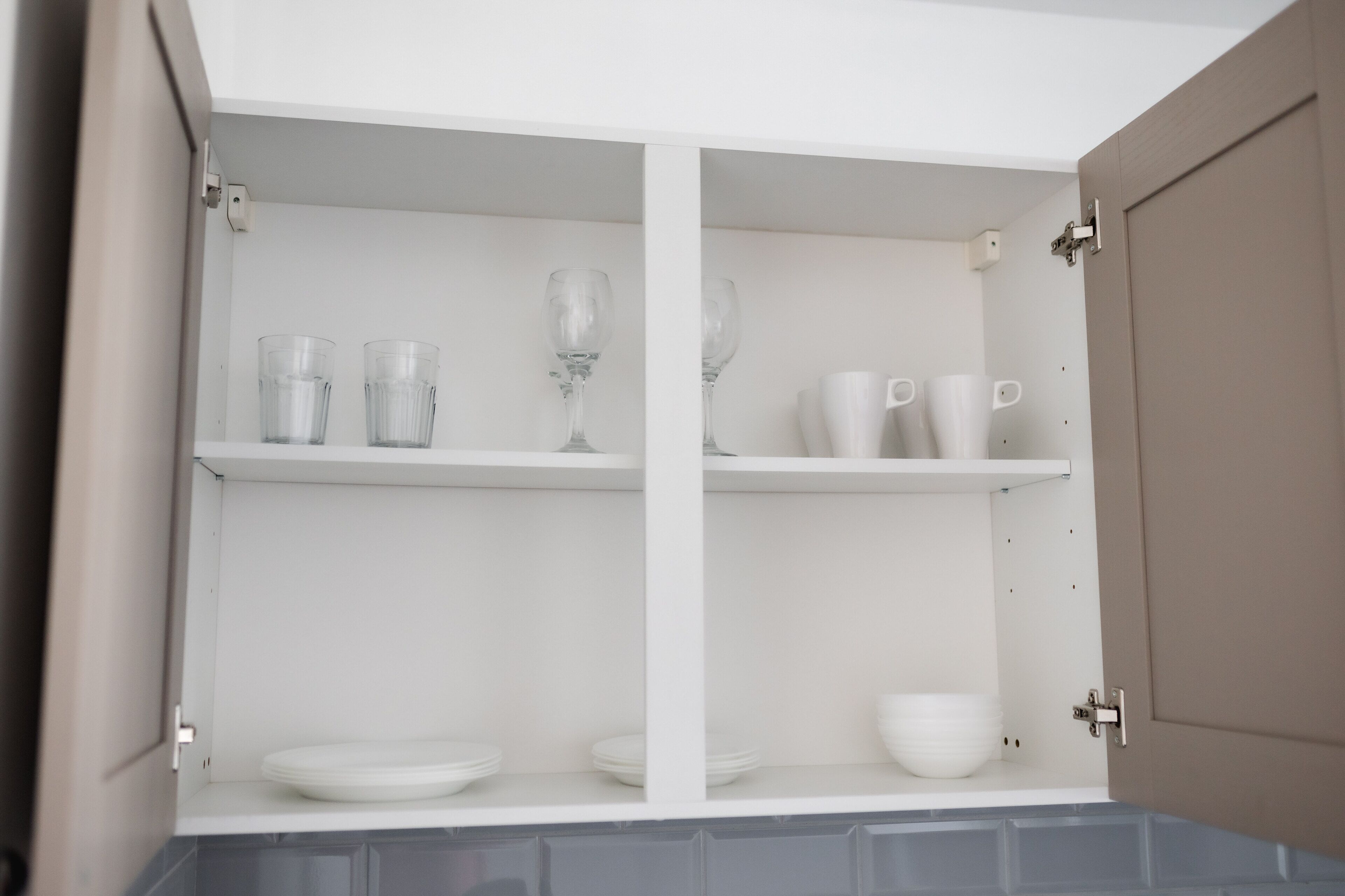 A kitchen cabinet with shelves holding plates, bowls, glasses, and cups.