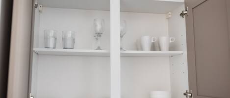 A kitchen cabinet with shelves holding plates, bowls, glasses, and cups.