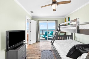 A bedroom with a TV, bunk bed, ceiling fan, and a balcony with chairs. - Gulf Front | Outdoor Shower | Dogs Allowed (Port St. Joe)