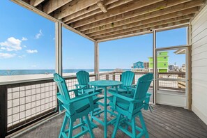 A covered outdoor area with a wooden ceiling, a table with chairs, and a view of the ocean and buildings. - Gulf Front | Outdoor Shower | Dogs Allowed (Port St. Joe)