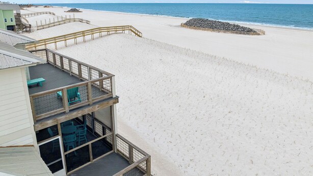 A beach view with a wooden deck, a building with a balcony, and a clear sky. - Gulf Front | Outdoor Shower | Dogs Allowed (Port St. Joe)