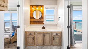 A bathroom with a wooden vanity, a round mirror, and a view of the ocean through a window. - Gulf Front | Outdoor Shower | Dogs Allowed (Port St. Joe)