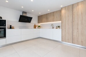 A modern kitchen with white cabinetry, a built-in oven, a microwave, and a flat-screen TV mounted on the wall. - VILLA LOS DADOS: 4 bedrooms, private pool, jacuzzi, and barbecue (Miami Playa)