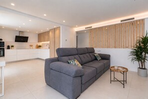 A modern living room with a grey sofa, a small wooden side table, and a potted plant. - VILLA LOS DADOS: 4 bedrooms, private pool, jacuzzi, and barbecue (Miami Playa)