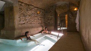 Piscina interna con pareti in pietra, con due persone che si rilassano nell'acqua.