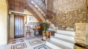 Un'ampia sala d'ingresso con pavimento piastrellato caratterizzato da motivi geometrici, una scala con ringhiera in ferro battuto e una parete in pietra rustica.