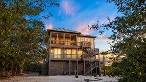A multi-story beachfront house with balconies, a staircase, and a sandy beach in the foreground. - Bay Front Escape w/ Dock and Gulf Views (Port St Joe)