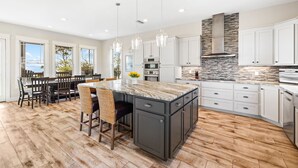 A modern kitchen with a large island, white cabinetry, and a stone backsplash. - Bay Front Escape w/ Dock and Gulf Views (Port St Joe)