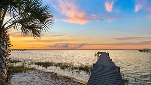 A wooden pier extending into calm waters, surrounded by sand and sparse vegetation. - Bay Front Escape w/ Dock and Gulf Views (Port St Joe)